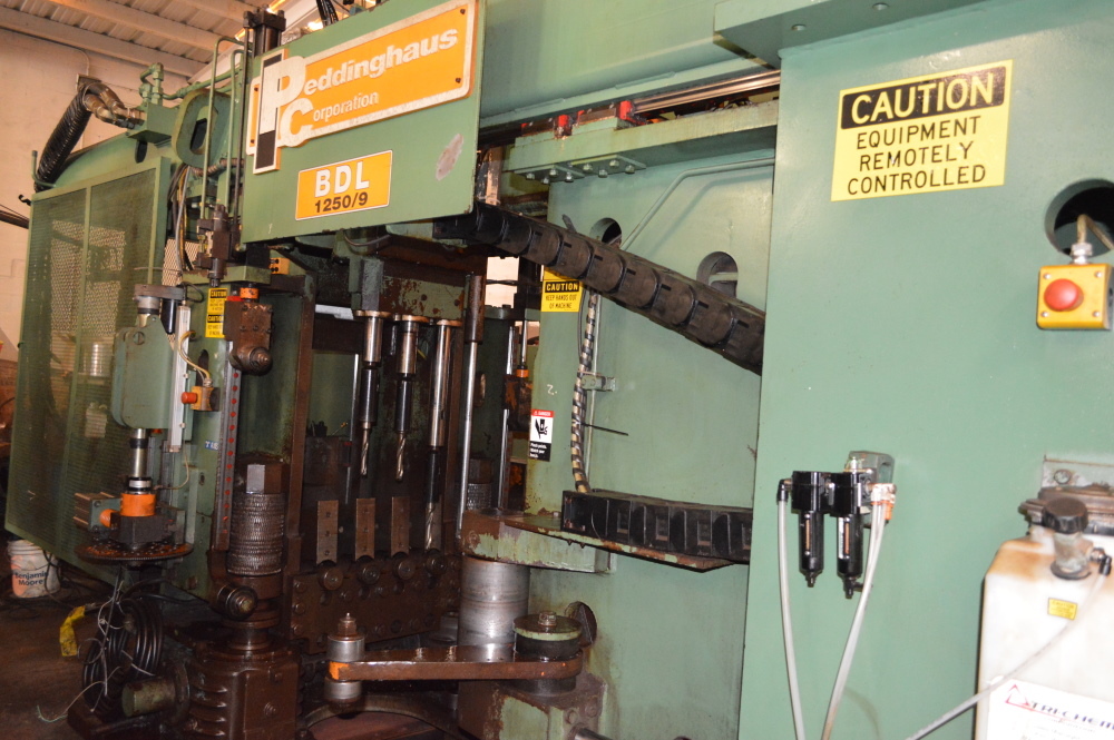 A green Peddinghaus BDL 1250/9 beam drill line with vertical drill spindles, orange nameplate and a yellow Caution Equipment Remotely Controlled sign.