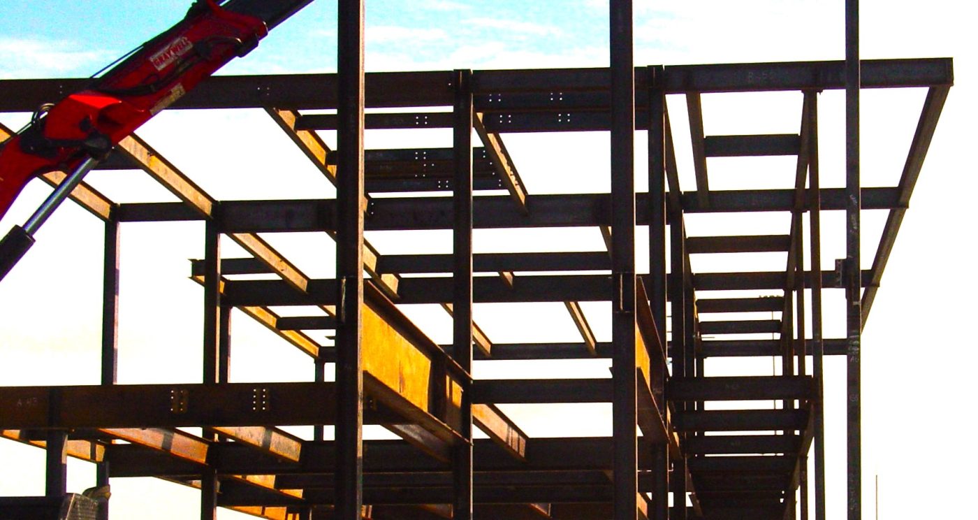 Columns, beams and stair framing of a steel building frame silhouetted against a bright sky.