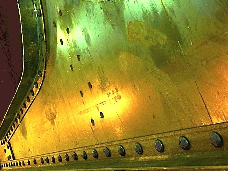 Rows of hot-driven rivets across a steel plate and along its angle flange, lit in warm workshop light.