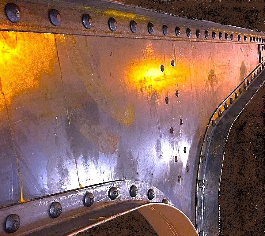 Close-up of a riveted steel gusset plate, rows of round rivet heads following the curved flange of a historic steel member.