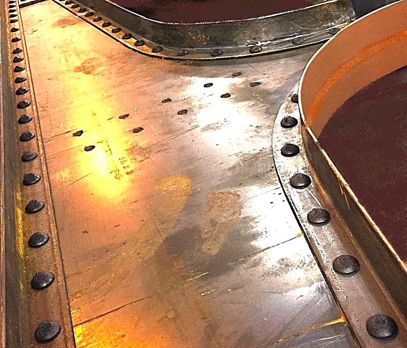 A riveted steel joint where curved flanges meet a flat plate, each seam closed with a line of rivet heads.