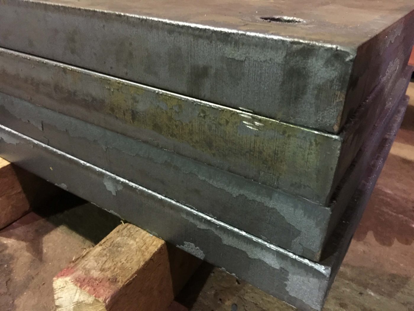 A close view of four flame-cut heavy steel plate strips stacked one on another with ground edges, resting on timber dunnage in a shop.