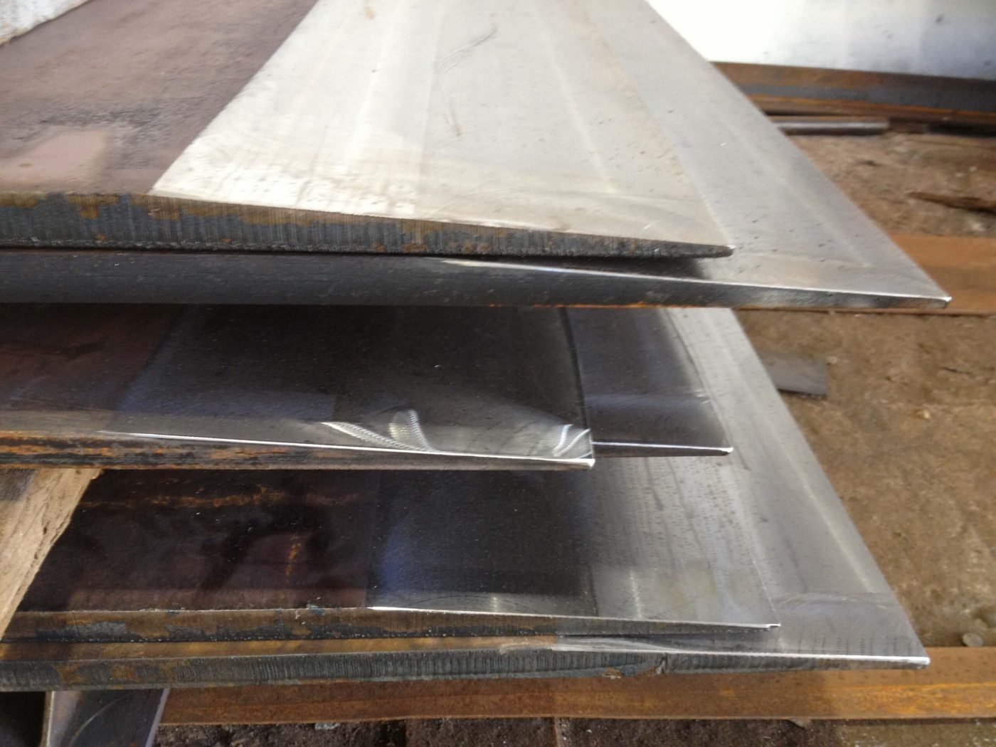 A close view of several steel plates stacked on timber blocking, their flame-cut and sheared edges facing the camera.
