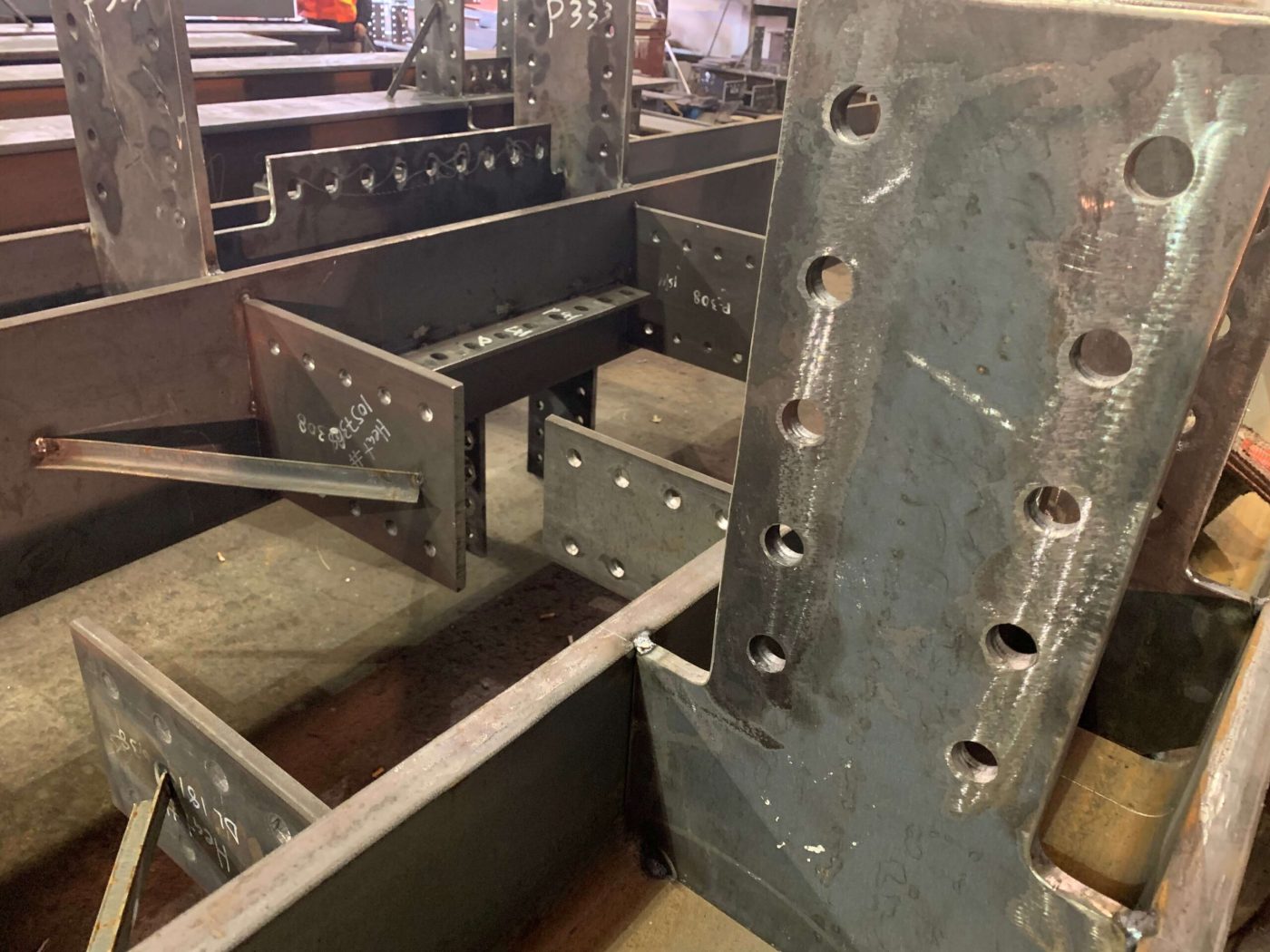 A close view of thick steel connection plates with drilled bolt holes and visible weld beads at the end of a fabricated beam.